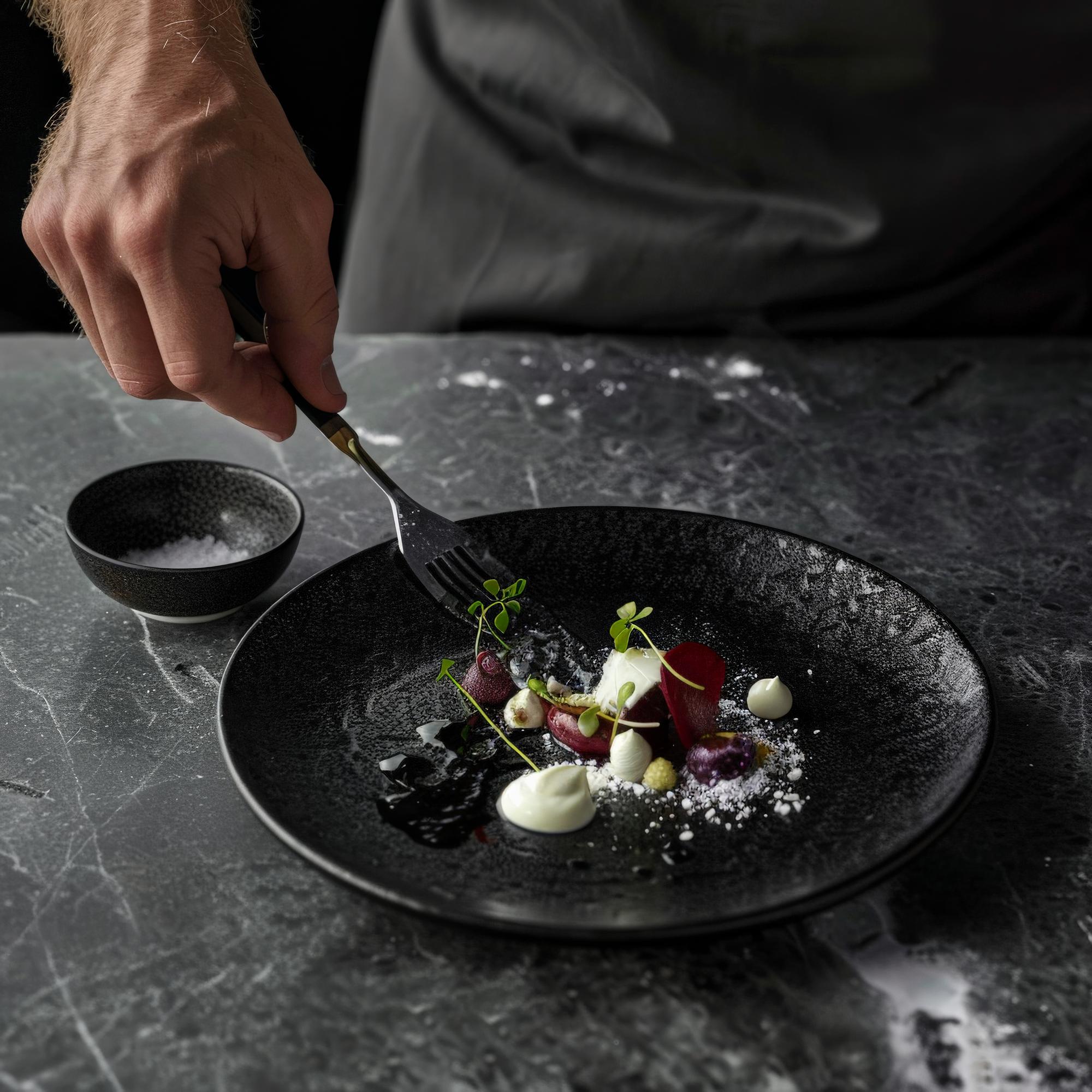 Chef arranging a plated gourmet dish on dark table